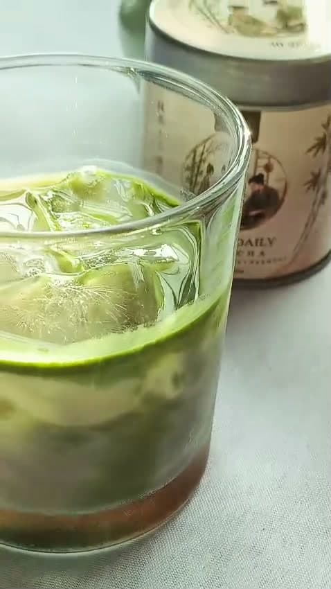 A finished iced SUKO matcha in a glass with ice and milk, beside the SUKO Daily Matcha tin