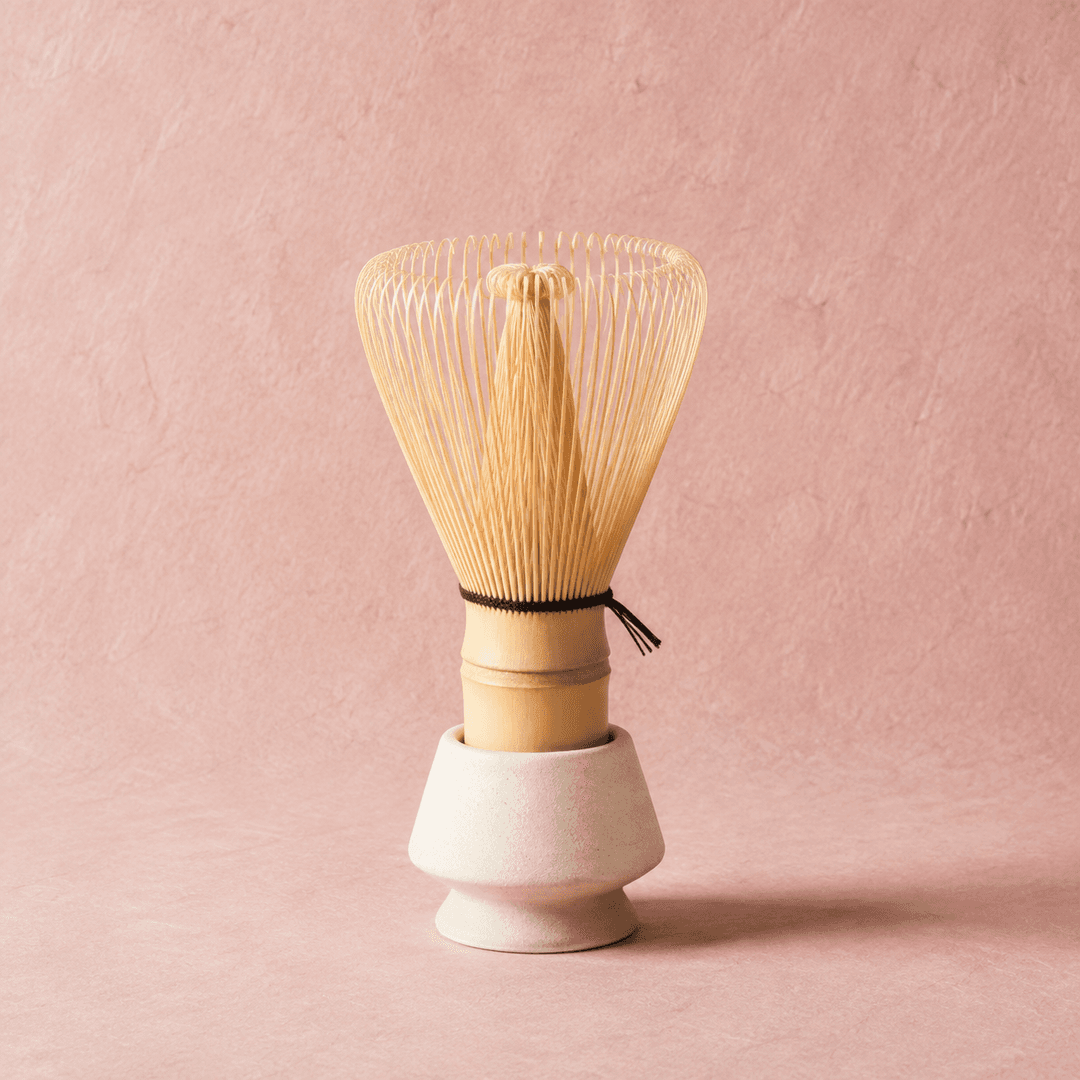 A bamboo matcha whisk (chasen) resting in a ceramic stand